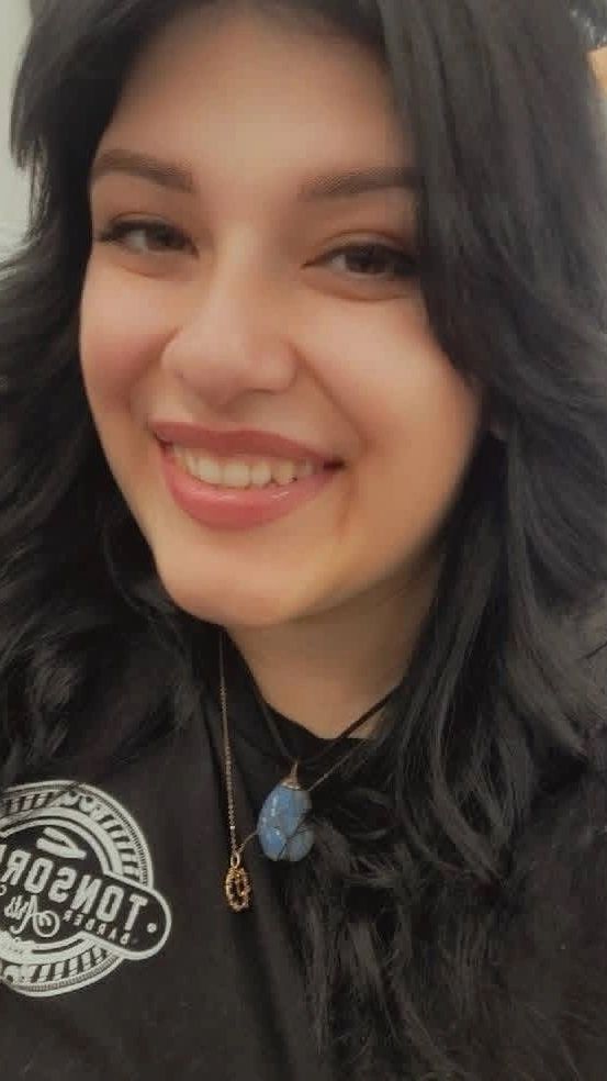 Smiling woman with dark hair and blue pendant necklace.
