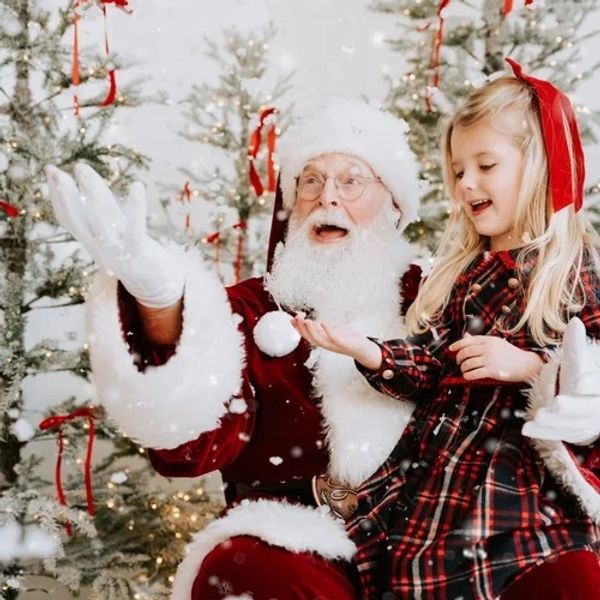 Santa Claus joyfully interacts with a little girl amid festive Christmas trees and falling snow.