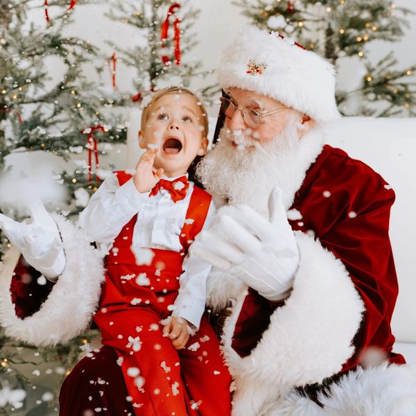 Excited child sitting on Santa's lap surrounded by festive Christmas decorations and falling snow.