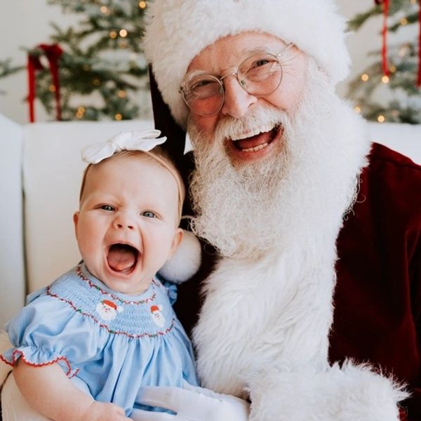 Baby joyfully sitting on Santa's lap, both smiling widely in festive setting.