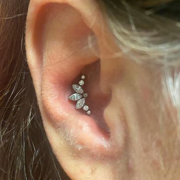 Close-up of an ear with a shiny, decorative cartilage piercing featuring multiple gems.