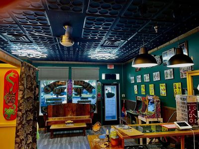 Tattoo shop interior with vibrant art, arcade games, and cozy seating.