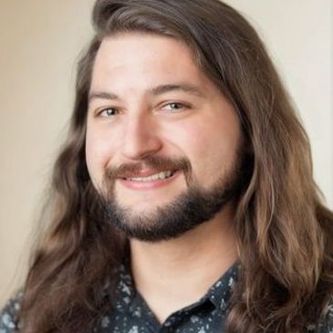 A smiling man with long hair and a beard in a patterned shirt on the website of a therapist for musicians, artists, writers, dancers, and other creative people.