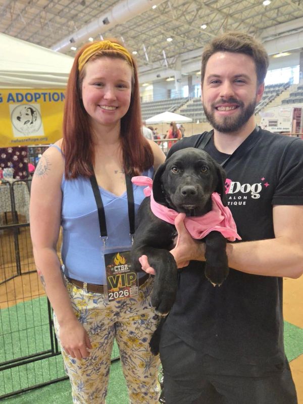 A smiling couple holding a black puppy at a pet adoption event.