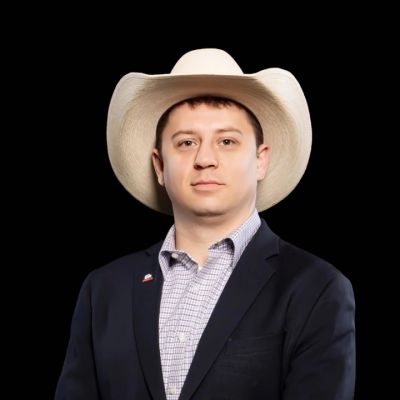 Man wearing a white cowboy hat and dark suit against a black background.