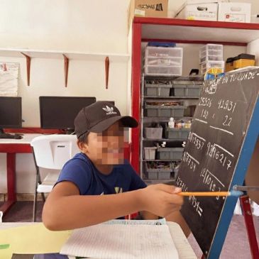 Niño señala números en una pizarra con lápiz en un aula.
