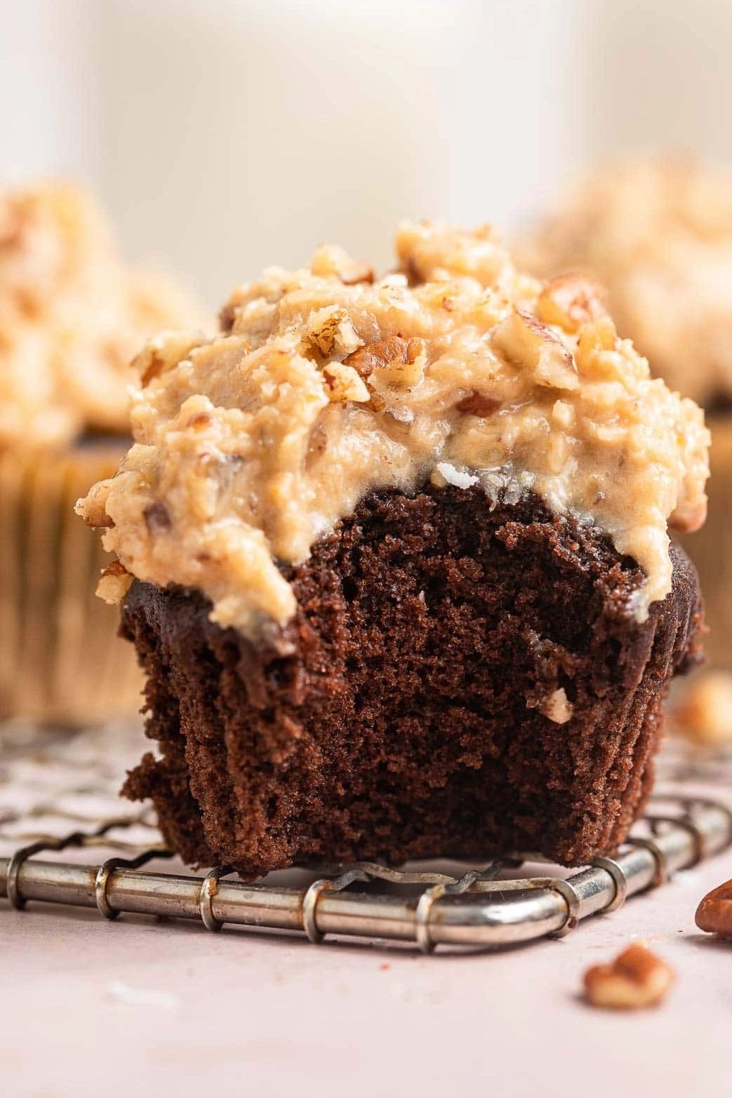 Chocolate cupcake with creamy frosting and chopped nuts, one with a bite taken out.