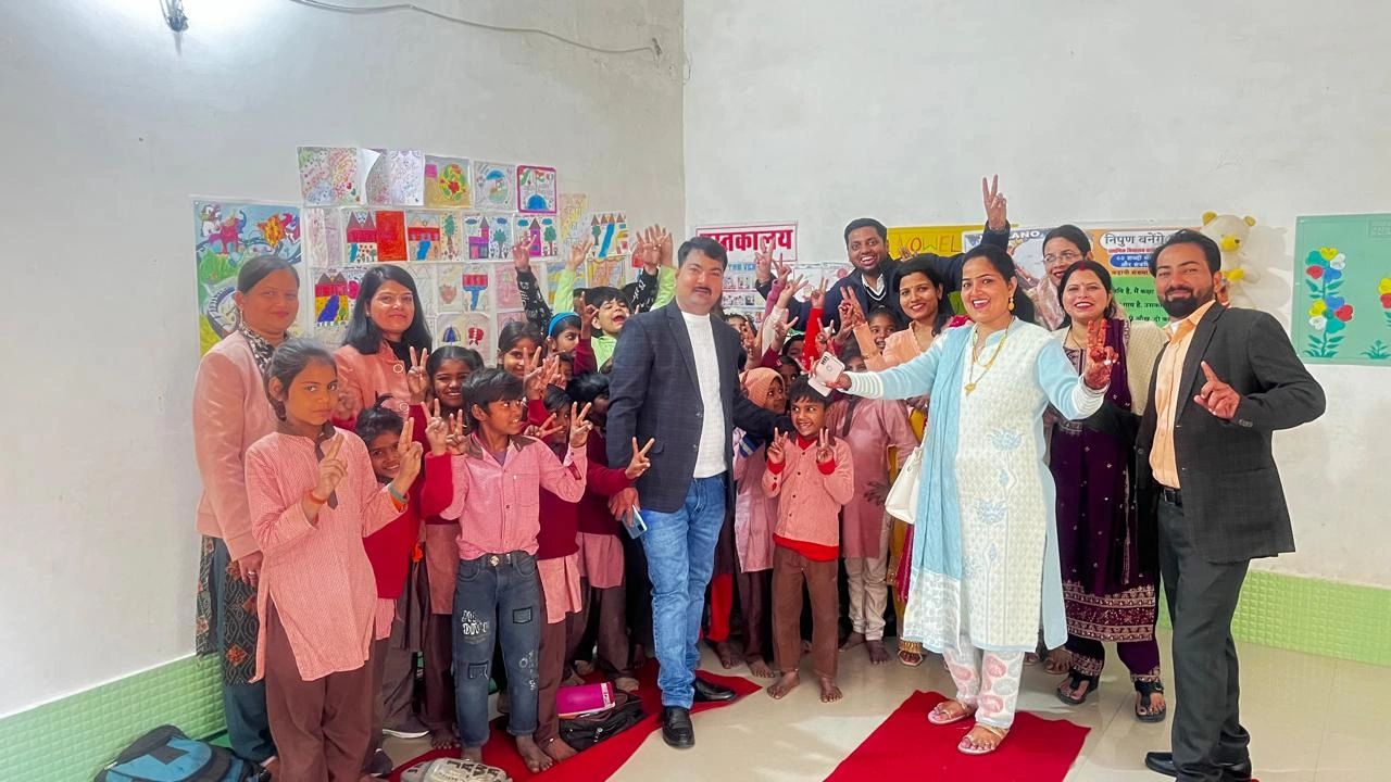 Group photo of children and adults showing peace signs in a classroom with colorful wall art.