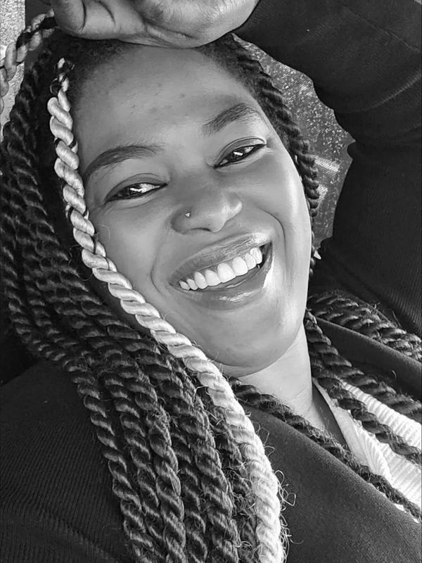 Close-up of a joyful woman with braided hair and a nose piercing, smiling brightly.