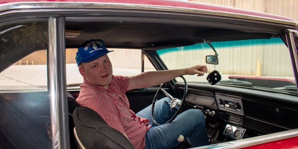 Young man in vintage car holding dice hanging from the rearview mirror.