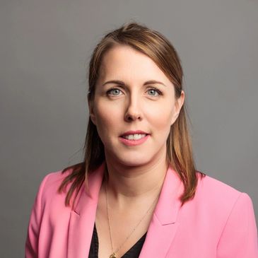 A tutor smiling at the camera wearing a pink blazer and black dress.