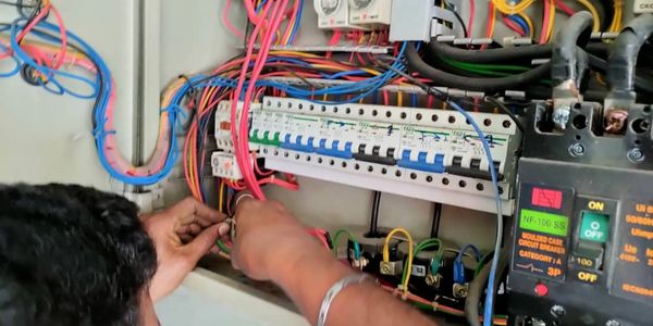 Electrician working on a complex circuit breaker panel with various colored wires.
