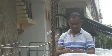 A man in a striped polo shirt stands outdoors near a building with air conditioners.