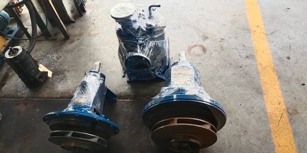 Three blue industrial pumps wrapped in plastic on a workshop floor.
