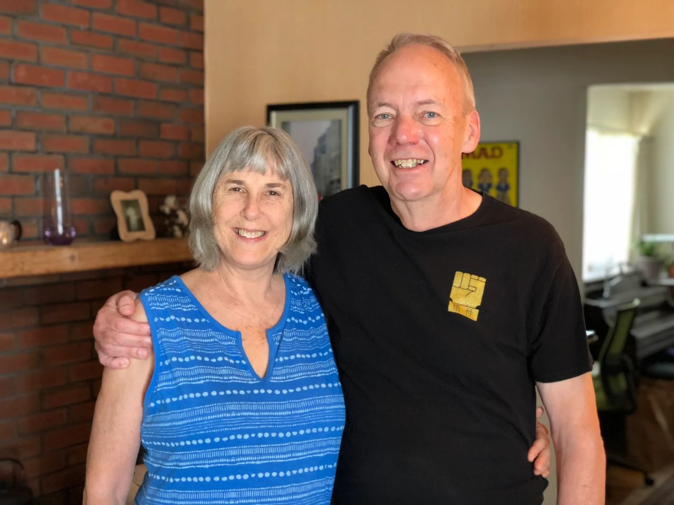 George Lawrence stands next to Chris Lawrence in their living room with his arm around her shoulder.