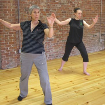 Two women holding the single whip posture.