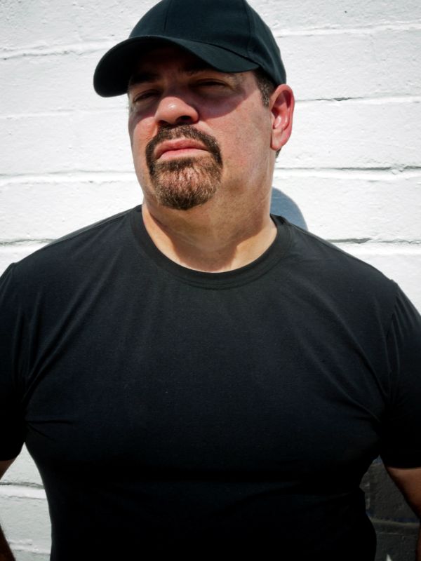 Man in black shirt and cap against white wall.