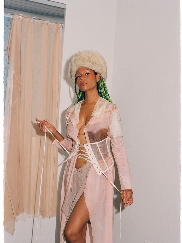 Woman in a pink outfit with green braided hair and a fur hat.