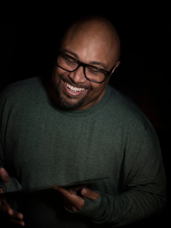 Man with glasses smiling warmly in dim lighting.
