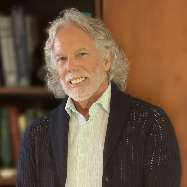 Smiling elderly man with white hair and beard wearing a dark cardigan.