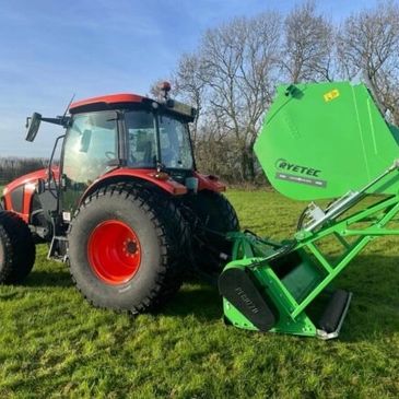 Red tractor attached to a green Ryetec agricultural machine on a grassy field.