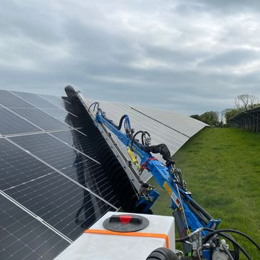 Machine cleaning solar panels outdoors on a cloudy day.