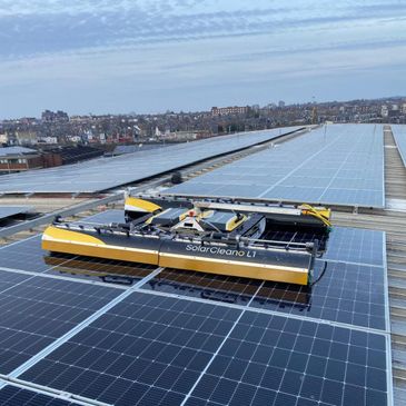 A robotic solar panel cleaner on a rooftop array under a blue sky.