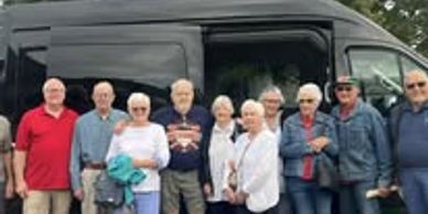 Group of elderly people posing in front of a black van.