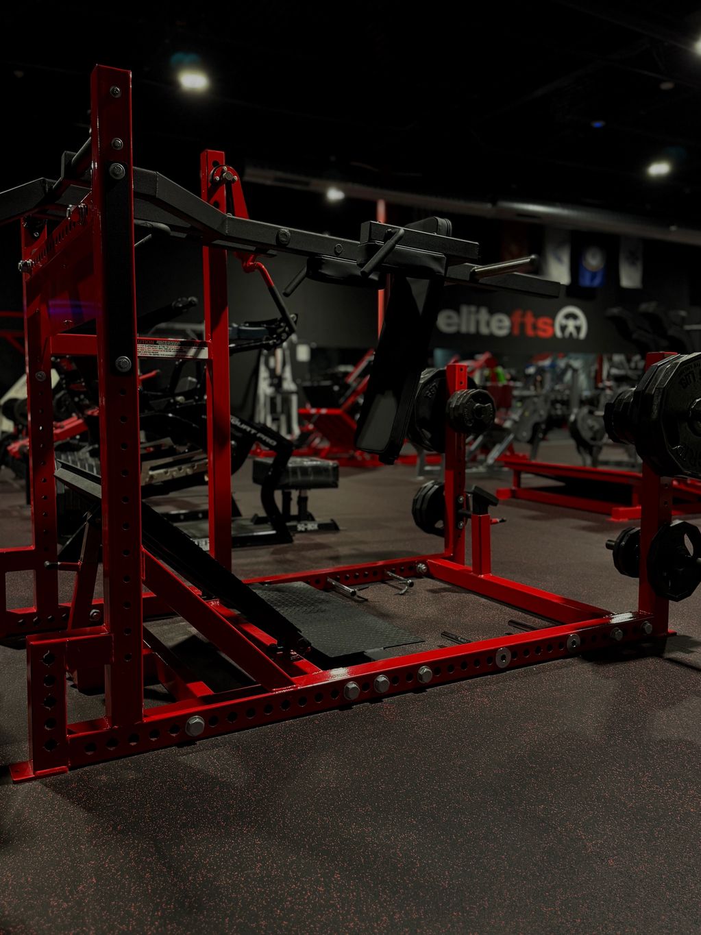 Red squat rack with weights in a dimly lit gym.