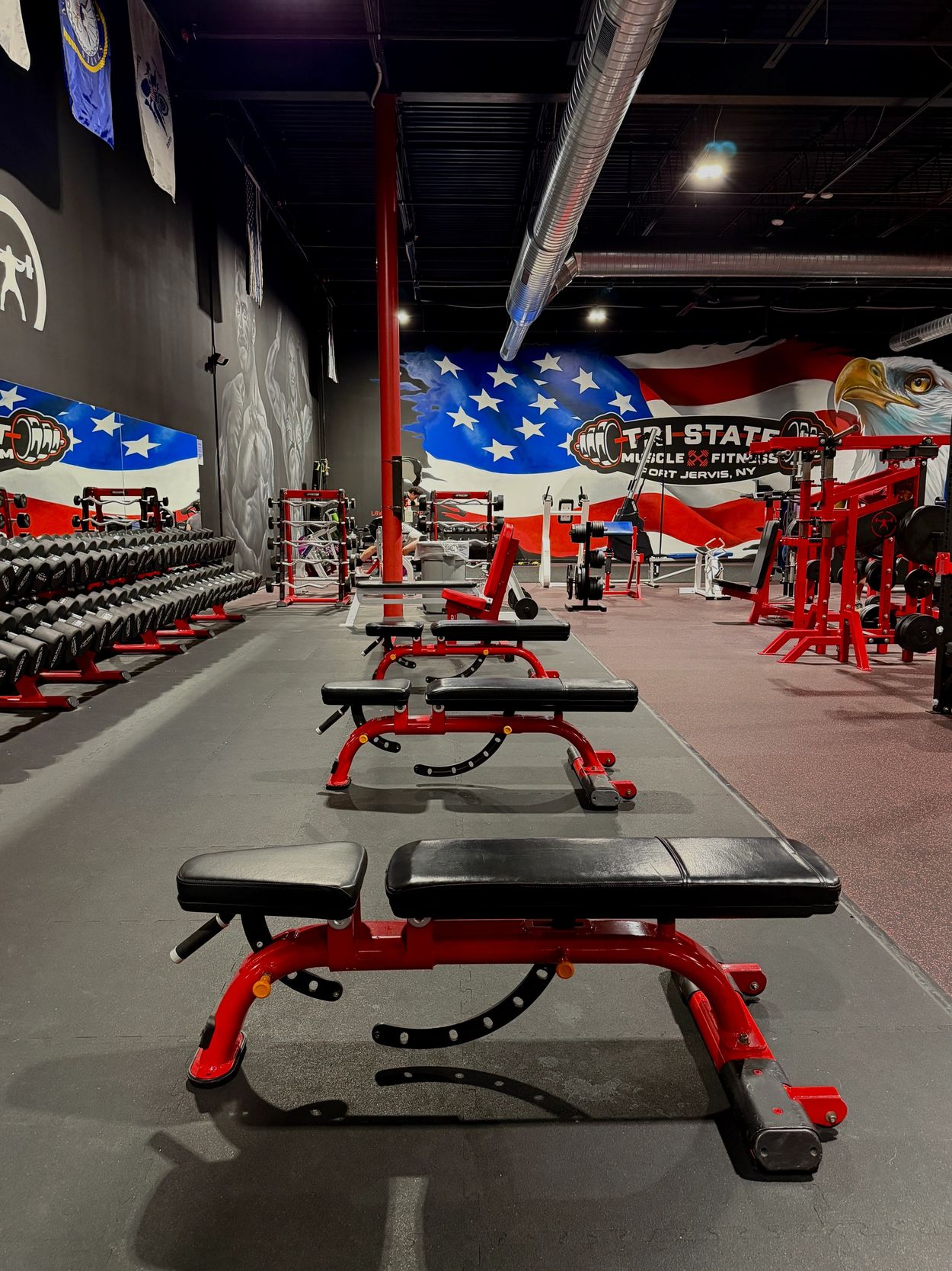 Empty gym with red workout benches and patriotic wall art.
