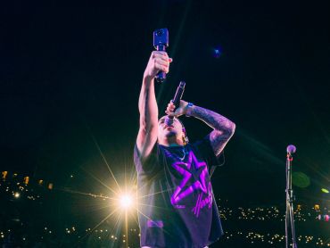 Cantante con micrófono y cámara en mano en un concierto.