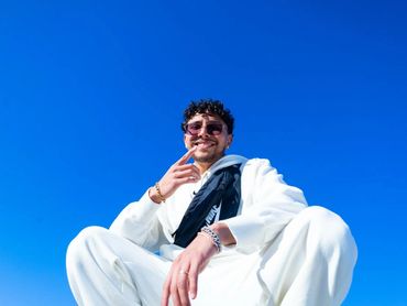 Hombre sonriente vestido de blanco bajo un cielo azul.