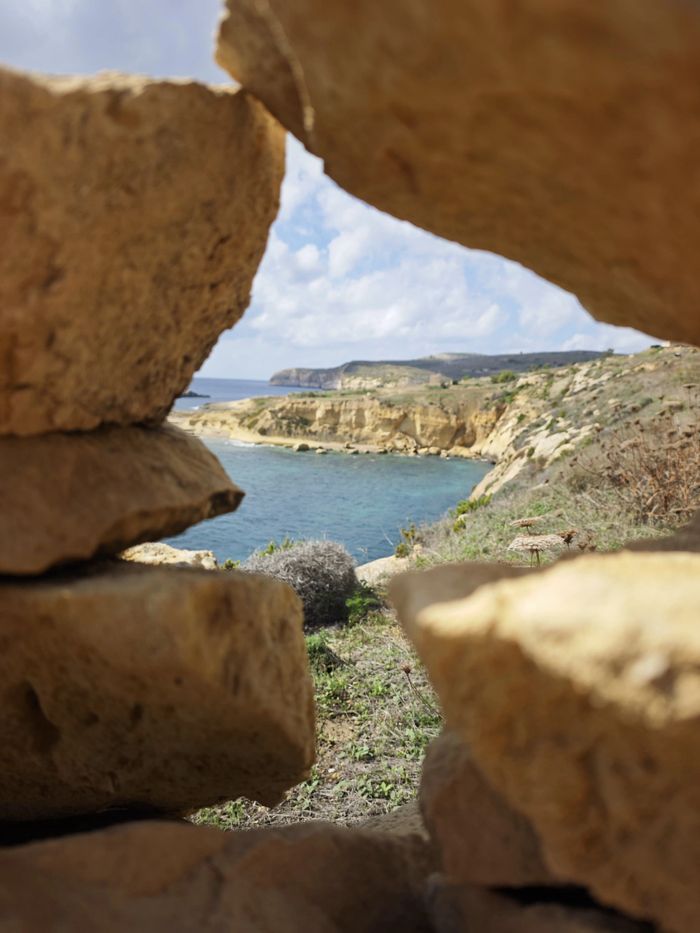 Coastal view framed by rugged rocks revealing blue sea and cliffs.