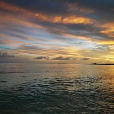A serene ocean view during a colorful sunset with scattered clouds.