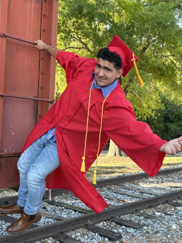 Graduate posing on a train track in a red gown.