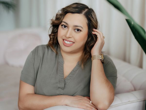 Smiling woman with wavy hair leaning on a white couch in a cozy room.