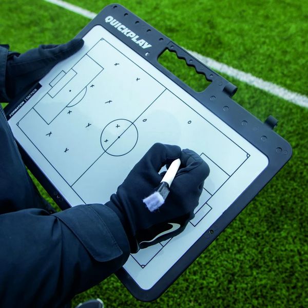 Coach holding a tactics board with player positions on a soccer field.