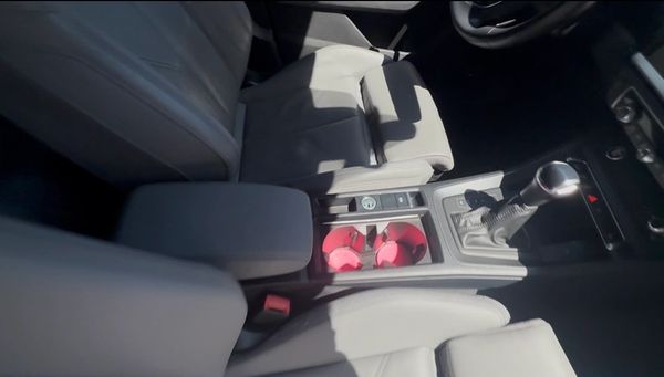 Car interior focusing on the center console with beige seats and pink cup holders.