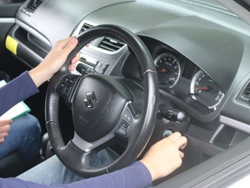 Person holding a Suzuki car steering wheel inside a vehicle.