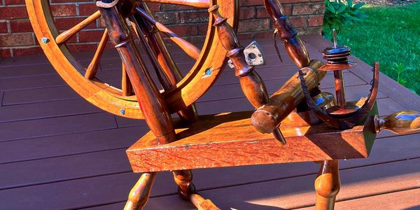 Vintage wooden spinning wheel on a porch deck in sunlight.