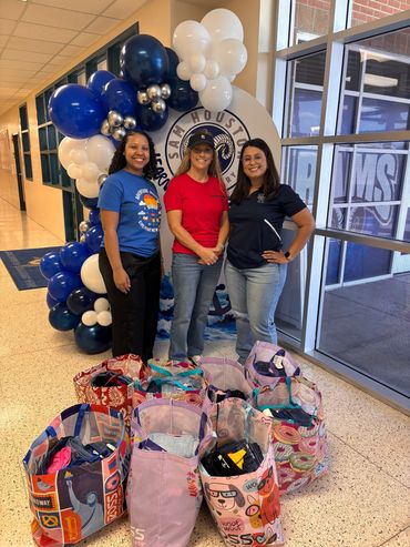 Three women posing indoors with bags and balloons.