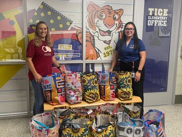 Two women standing with colorful bags of supplies in a school hallway.
