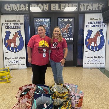 Two women standing inside a school lobby with bags on the floor.
