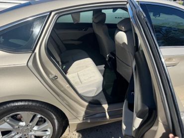 Open car door showing backseat of a beige sedan.