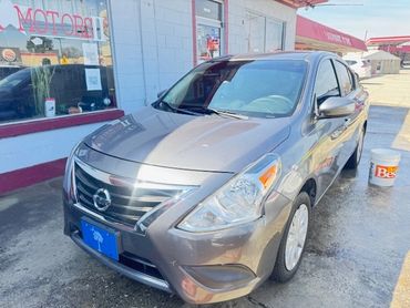 A gray Nissan sedan parked outside a building with a bucket nearby.