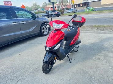 Red and black scooter parked on a concrete surface near cars.