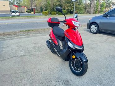 Red and black scooter parked on a driveway near a road.