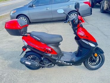 Red and black Accera scooter parked on pavement near cars.