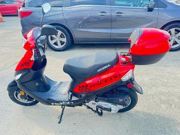 Red and black Ascenda scooter parked next to a gray car.
