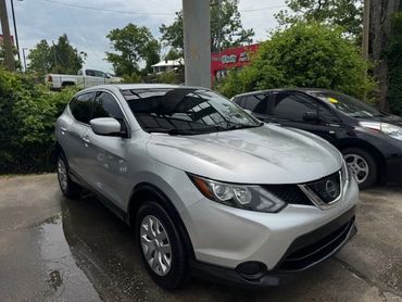 Silver Nissan SUV parked outdoors near greenery and another black car.